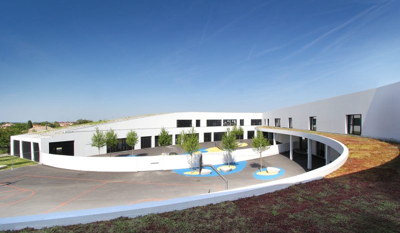 Photographie depuis l'étage depuis la toiture végétalisé, on voit l'auvent courbe et en bas, la cour d'école organisée en deux espaces séparées