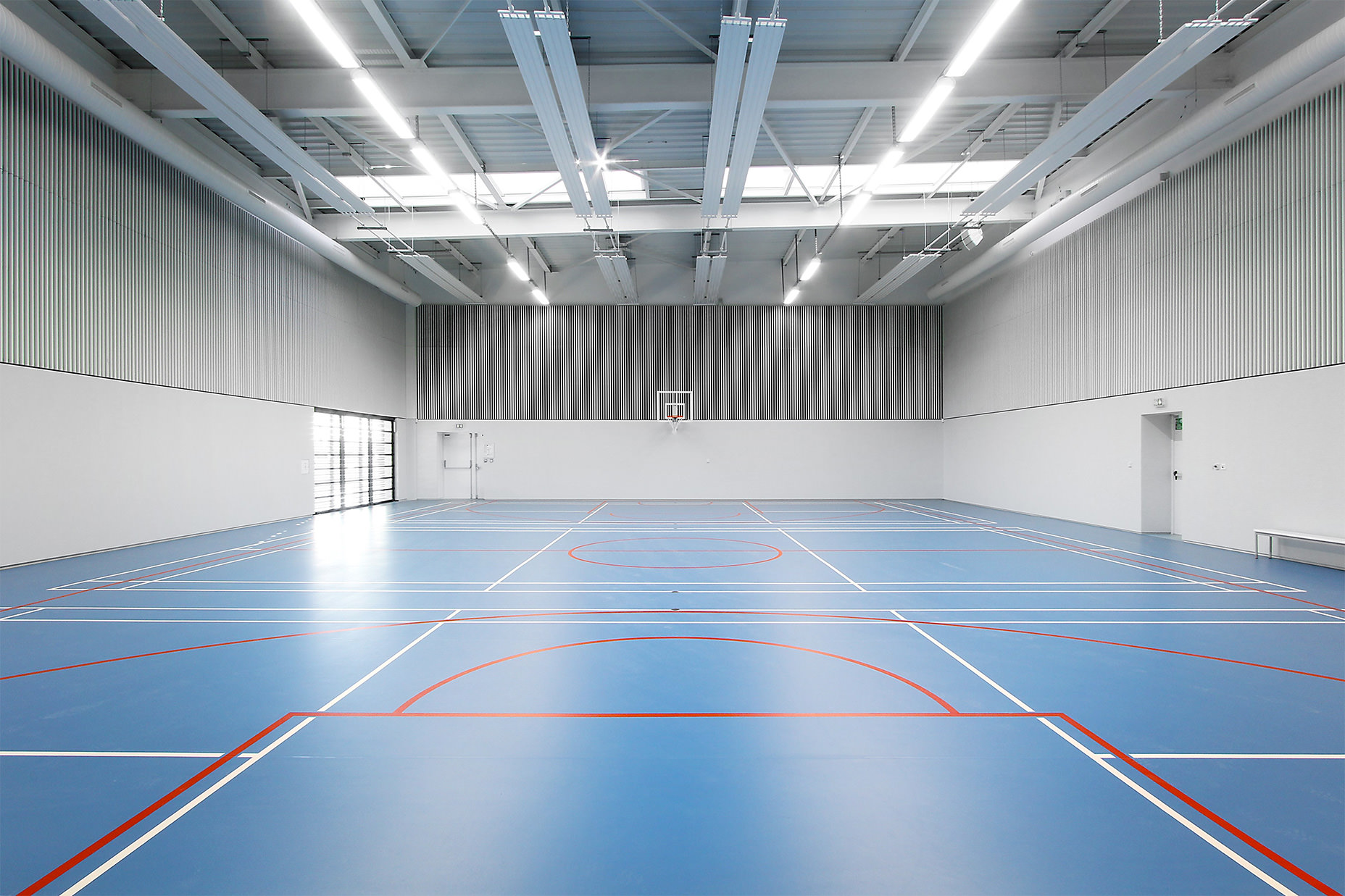 Photographie du gymnase intérieur, sol bleu lisse et mur béton et bardage vertical