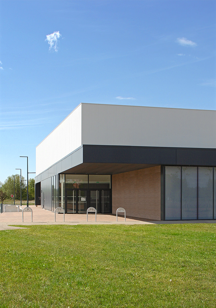 Photographie de l'entrée du bâtiment, auvent anthracite et mur en briquettes