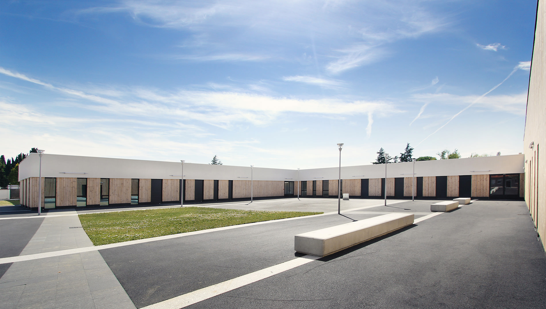 Photographie de la cour du lycée en forme de U, entourée de salle de cours, la partie supérieur est un bandeau blanc et inférieur vitres et bois