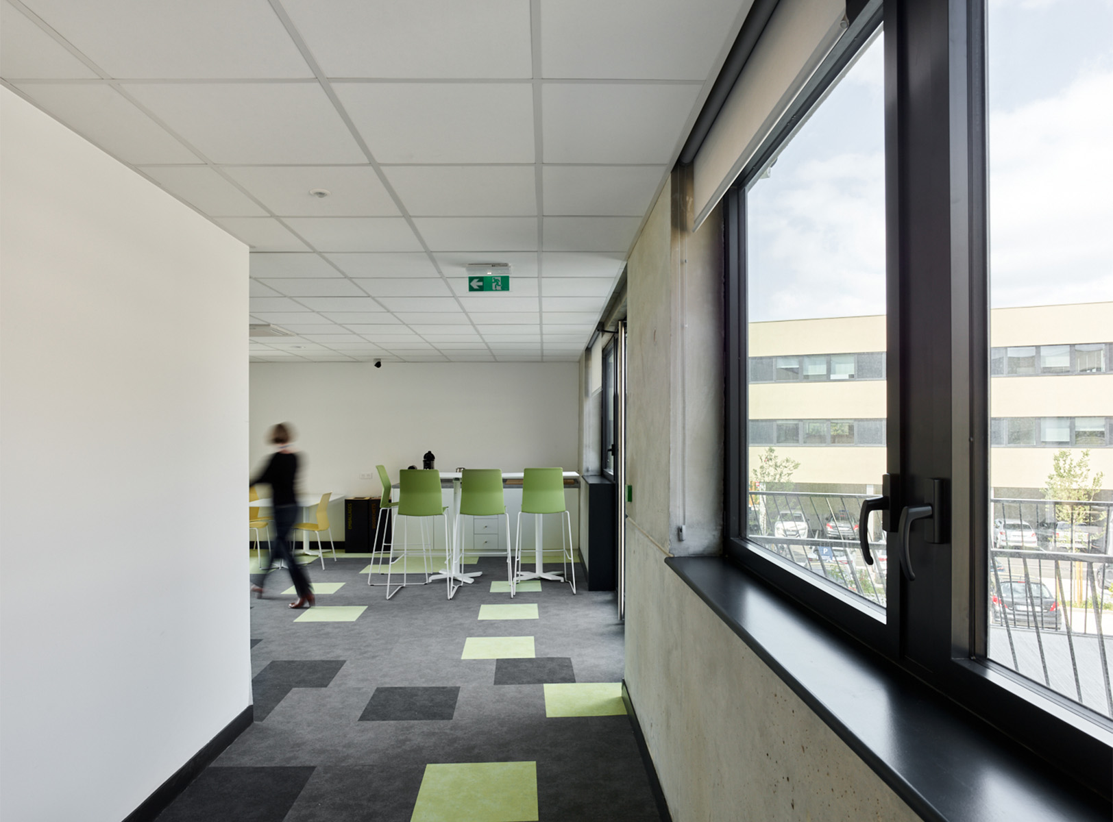 Photographie d'un espace de vie intèrieur depuis les fenêtres bandeaux, mur intèrieur beton brut, menuiserie gris anthracite et murs blancs