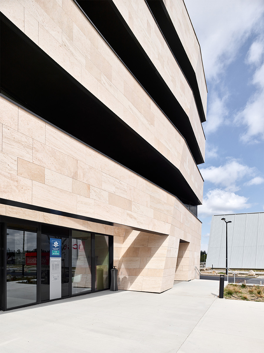 Photographie en contre-plongé de l'entrée du bâtiment perspective des 3 bandeaux balcons gris anthracite et des murs en pierre