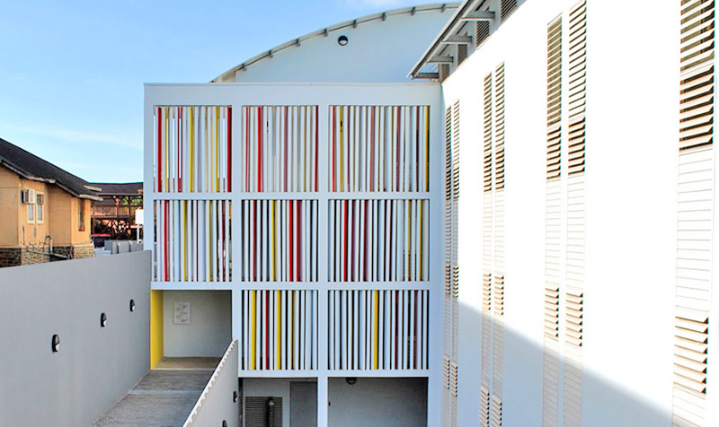 Photographie d'une entrée du bâtiment avec ventelles en béton verticaux rouge jaune blanc sur toute la hauteur des trois niveaux