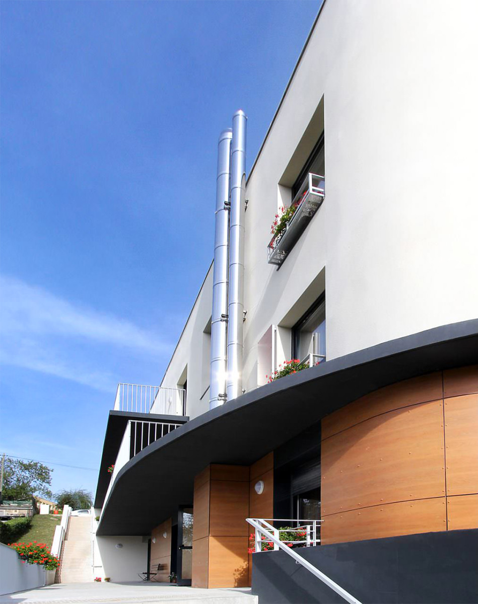 Photogrpahie d'un angle reconnaisable du bâtiment arrondi, enduit blanc, auvent anthracite et soubassement bois