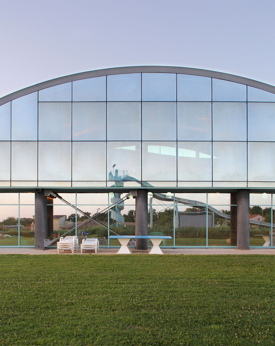 Photographie verticale face à la baie vitrée à l'endroit ou la structure de la toiture forme un dôme, pelouse tondue