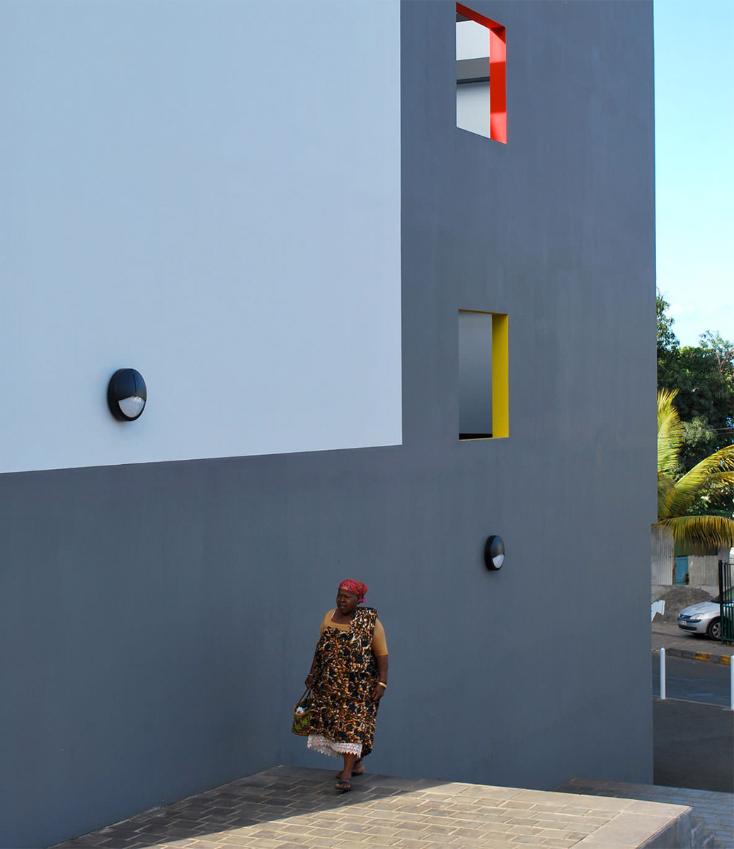 Photographie d'une personne marchant le long de la façade grise avec les ouvertures colorées