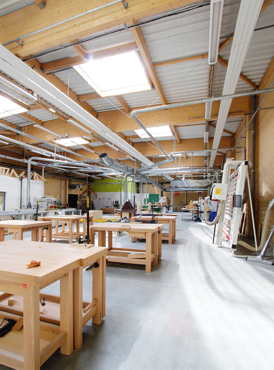 Photographie verticale d'intérieure d'une salle de cours technique avec un alignement de tables d'ateliers et d'outillage sur les côtés