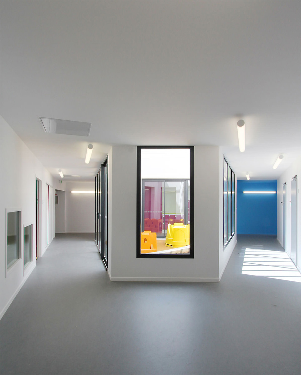 Photographie de deux couloirs, l'un bleu et l'autre blanc, qui se rejoingnent et au milieu un patio extérieur,