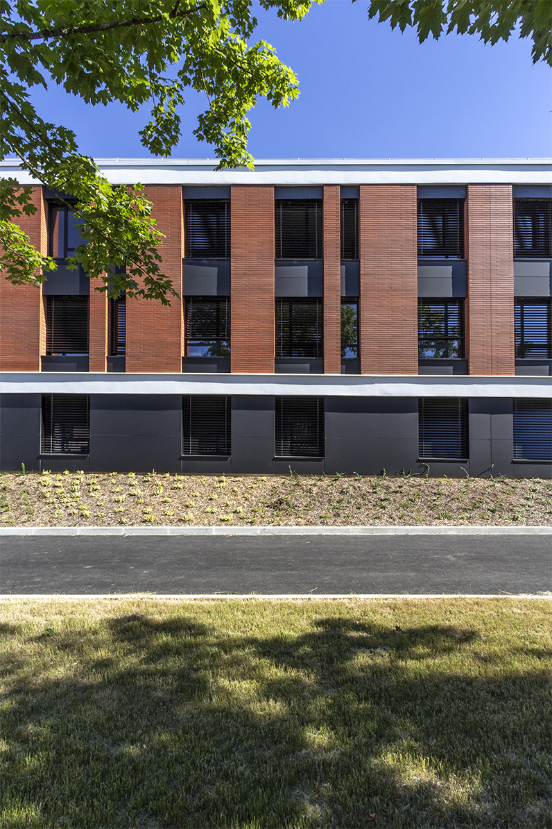 Photographie face à la voierie et la facade depuis l'espace vert, bâtiment brique encadrement blanc et soubassement gris anthracite