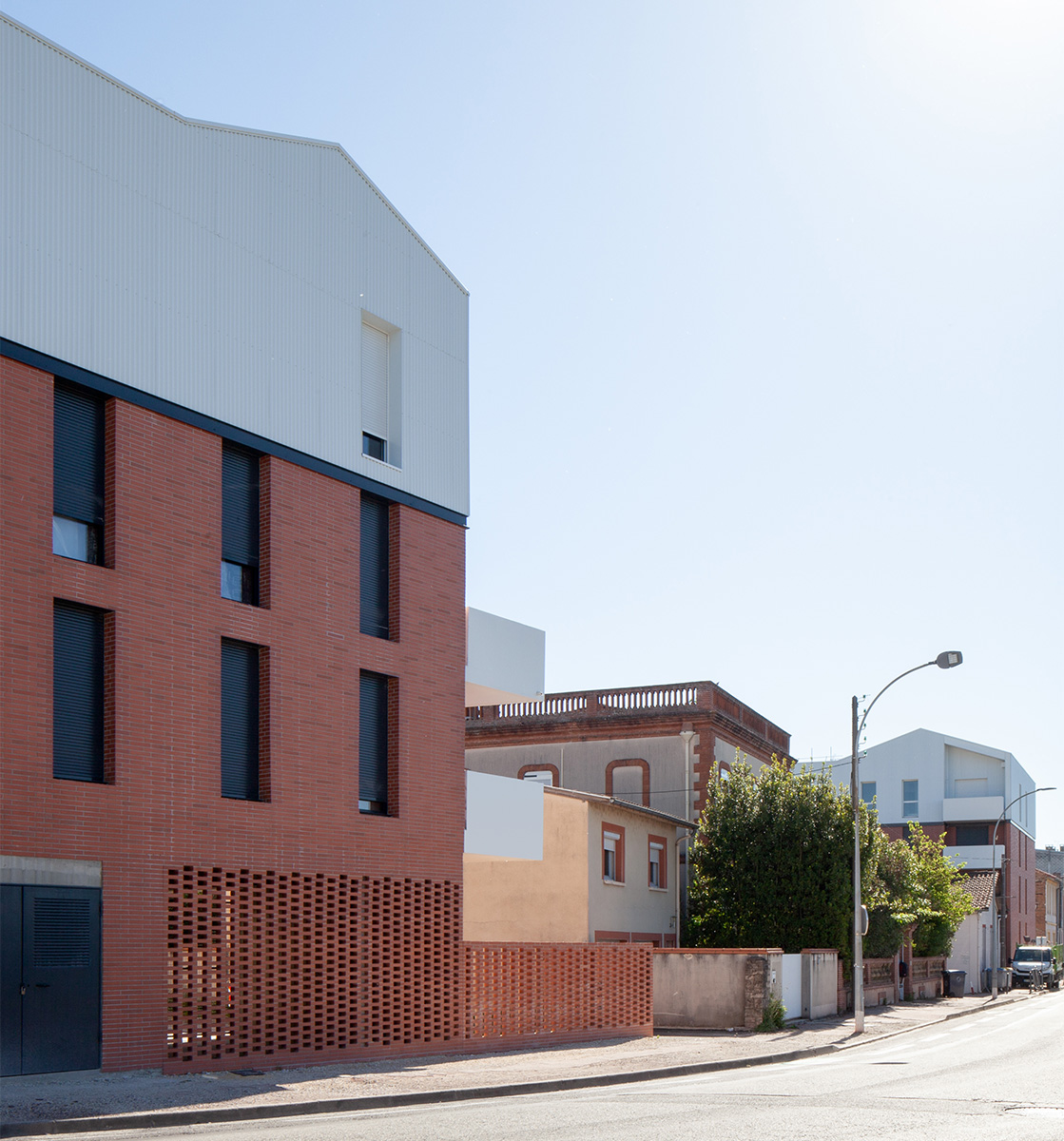 Photographie depuis la rue en enfilade, deux bâtiment de l'ilôt se font face, entre, des maisons existantes voient leur quartier changer