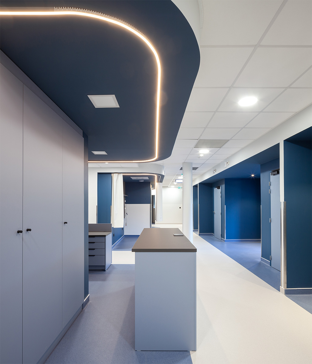 Photographie vue sur un croisement d'un couloir avec différents espaces délimitées par une couleur bleu au sol, table avec chemin lumineux au plafond