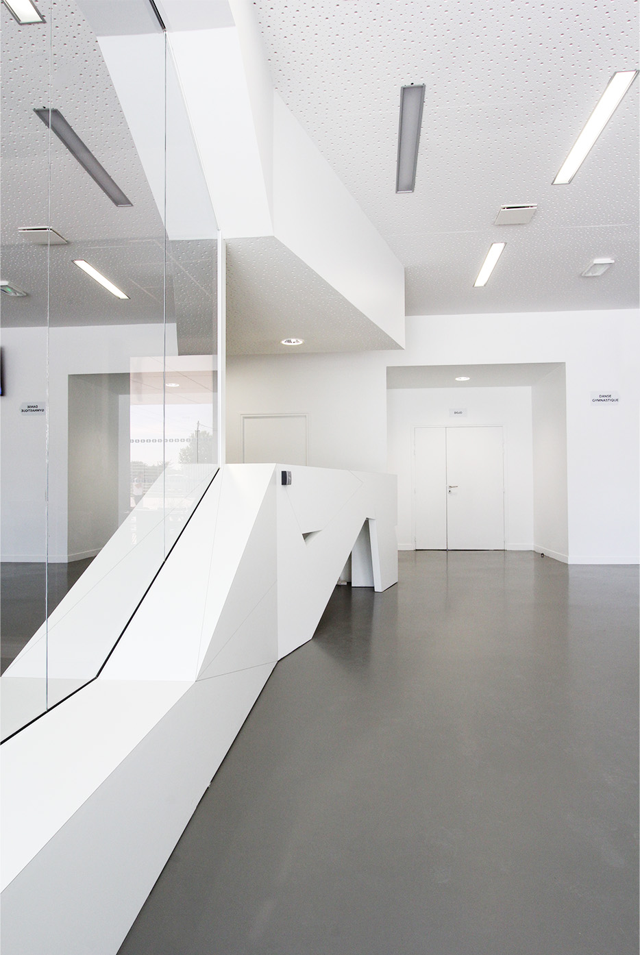 Photographie du hall d'accueil aux teintes minérales, sol béton lisse gris, murs et plafonds blancs et un pans de mur miroir
