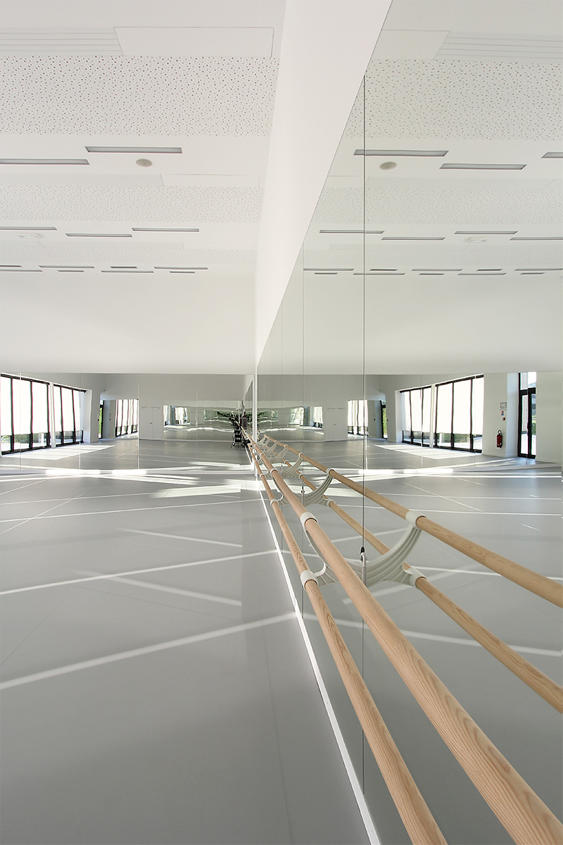 Photographie d'intèrieure d'une salle de danse ou de cours divers avec tout un pans du mur en miroir face à la baie vitrée