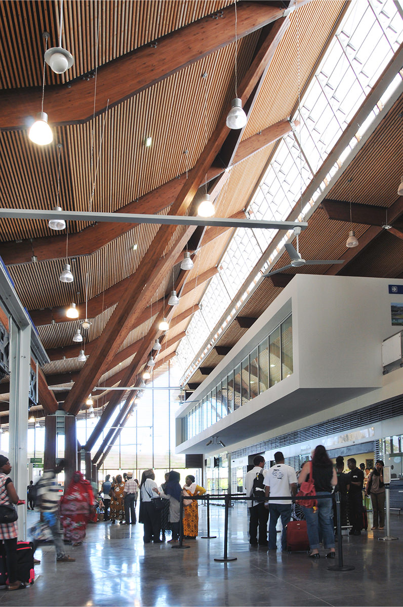 Photographie du hall au centre du bâtiment avec l'ouverture de la toiture sur toute la longeur qui apporte de la luminosité, lames et poutres en bois au plafond