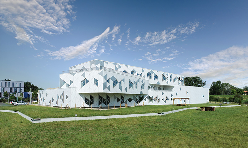 Photographie de 3/4 depuis le jardin des différentes faces blanches enboitées les une dans les autres, fenêtres et motifs triangulaire en façade se repondent sur deux étages