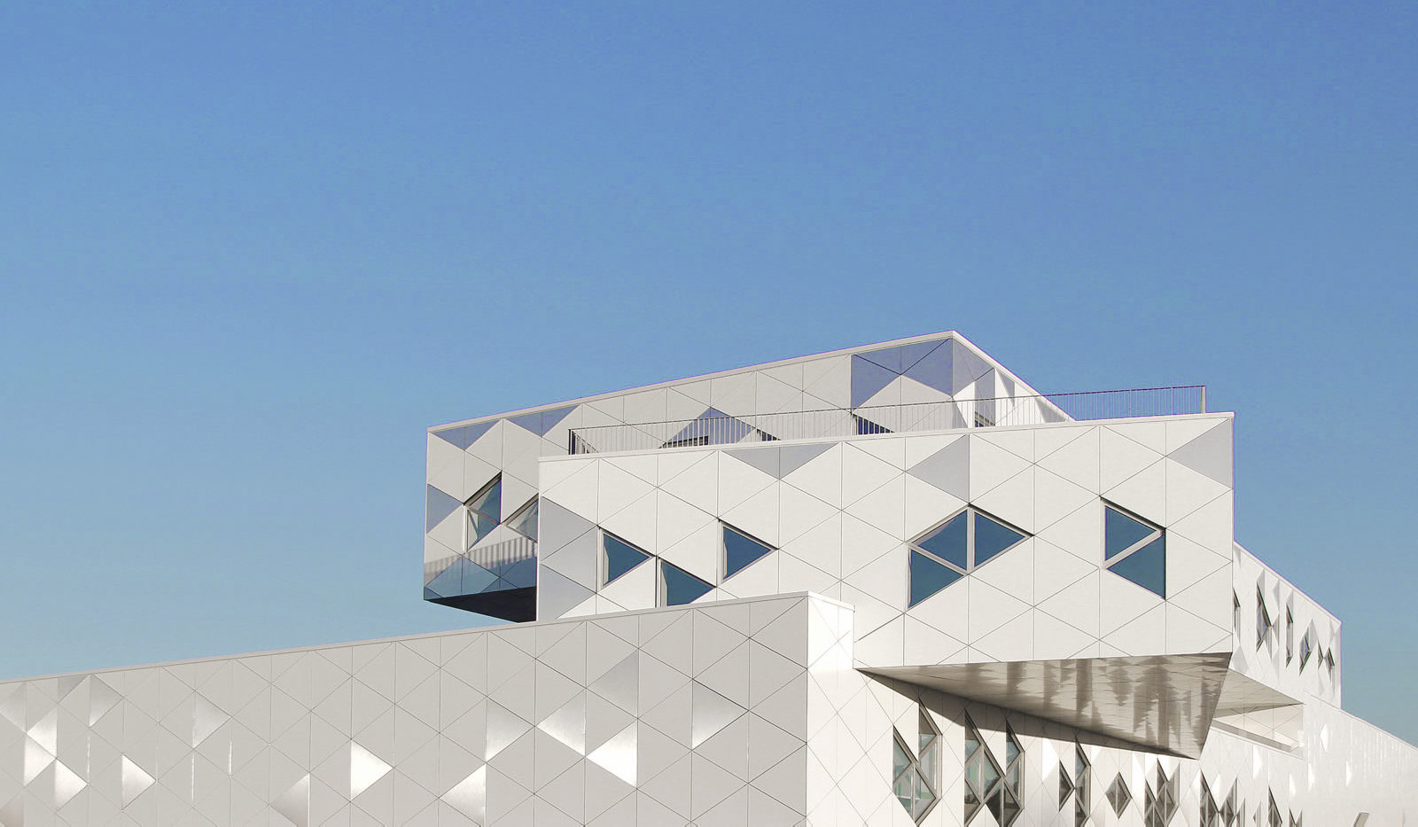 Photographie cadrée sur le haut du bâtiment de ETERA, vue en contre-plongée sur les 3 volumes superposés mais non-alignés, fenêtres et motifs sur la facade blanche de la même taille triangulaire