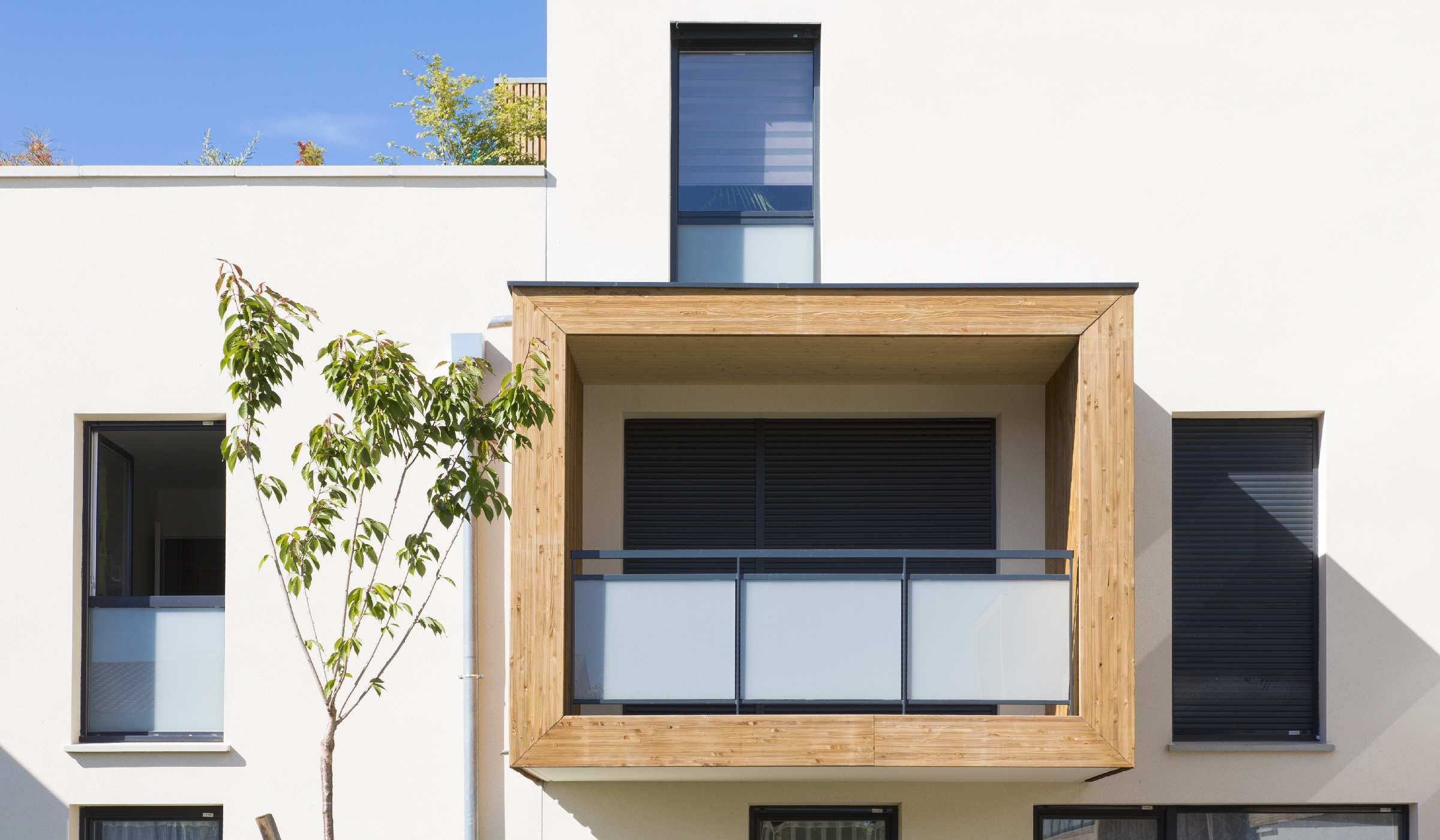 Photographie détail d'un balcon encadré de bois qui sort de la facade blanche au soleil