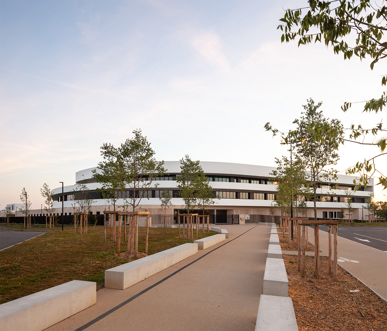 Photographie du parvis de Guilhermy à Toulouse avec son alignement de bancs béton et de part et d'autre l'herbe et les arbres plantés commencent à pousser