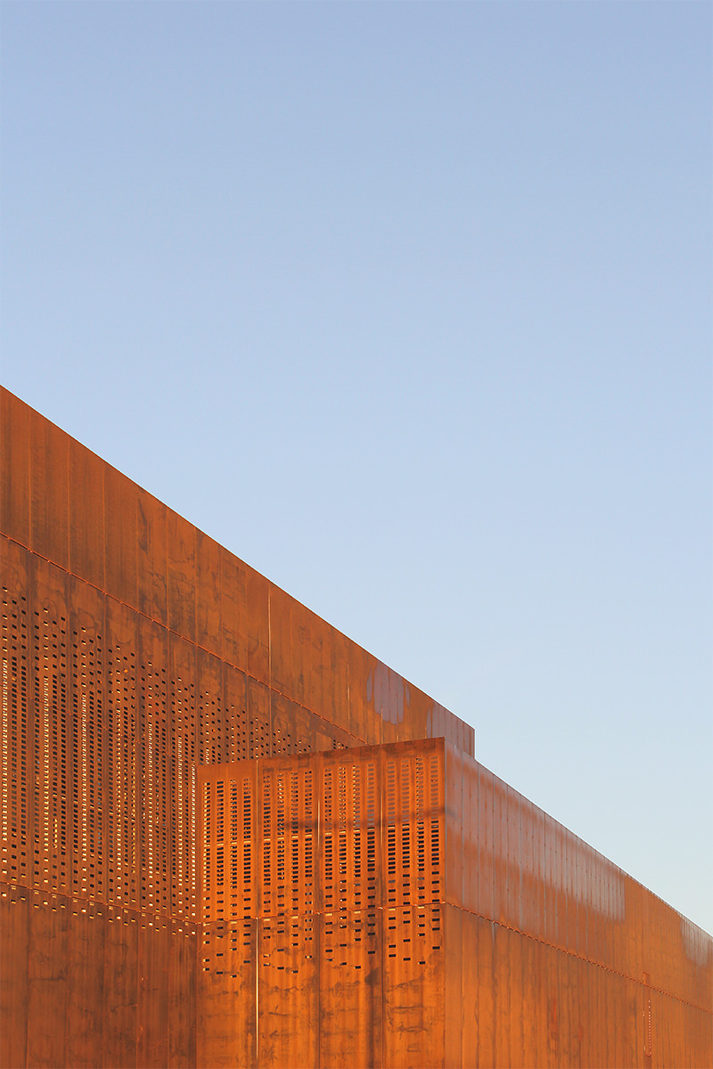 Photograhphie d'un détail de la façade avec vue sur les perforations dans le corten rouillé couleur ocre