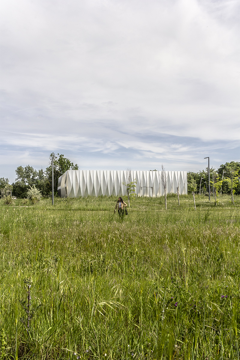 Photographie de la facade gris blanche triangulaire refléchissante dans son contexte arboré