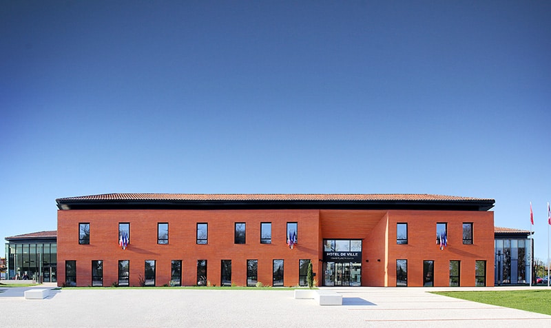 Photographie de l'hôtel de ville de Mondonville R+1, facade principale depuis le parvis minéral, matériau unique brique et une entrée en renfoncement de biais comme un grand porche d'entrée tout hauteur