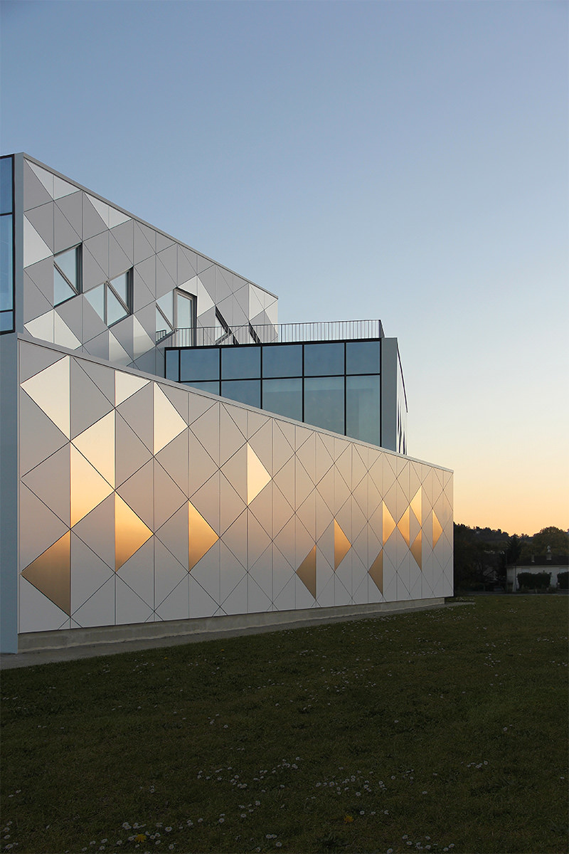 Photographie verticale de la façade qui refléte le coucher de soleil sur les facettes triangle d'Ariane Network
