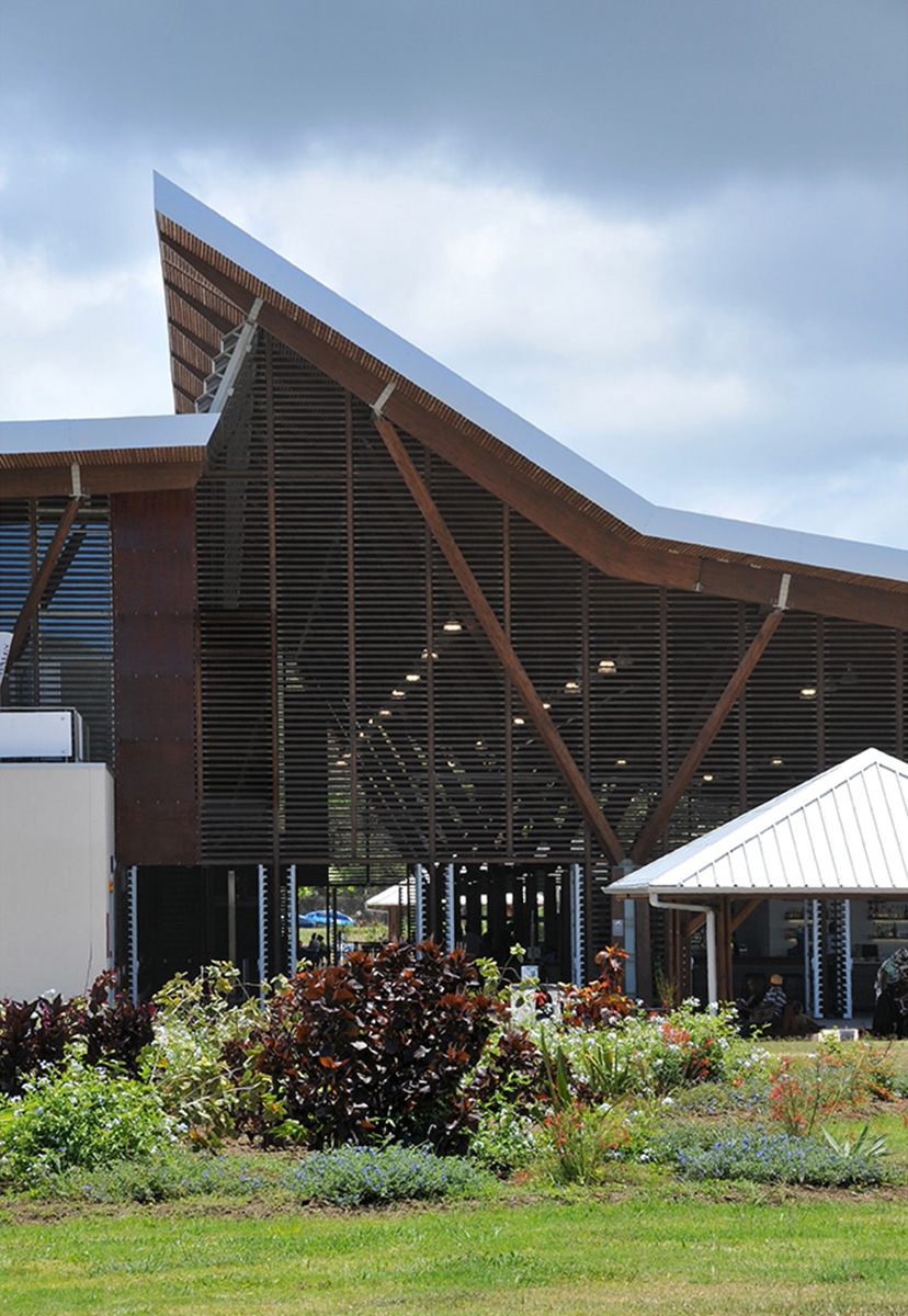 Photographie du plus haut de la façade entres les deux pentes de toit, les lames de bois du hall laissent apercevoir l'espace vert extérieur