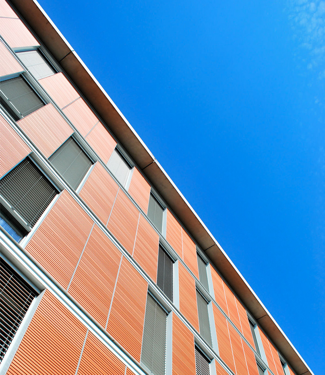 Photographie en contre plongé de la façade couleur brique avec vue sur le ciel bleu