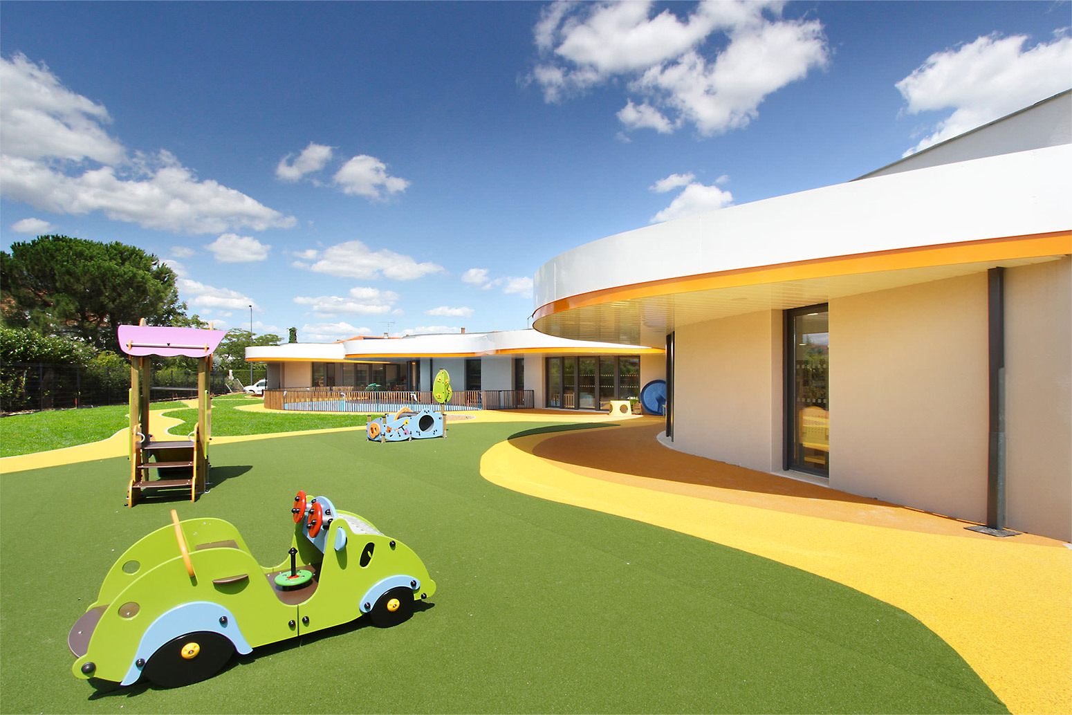 Photographie de la grande cour avec sol vert jaune et orange et des jeux pour enfants