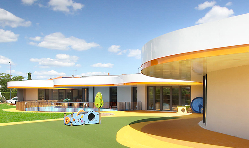 Photographie de la grande cour avec sol vert jaune et orange et des jeux pour enfants