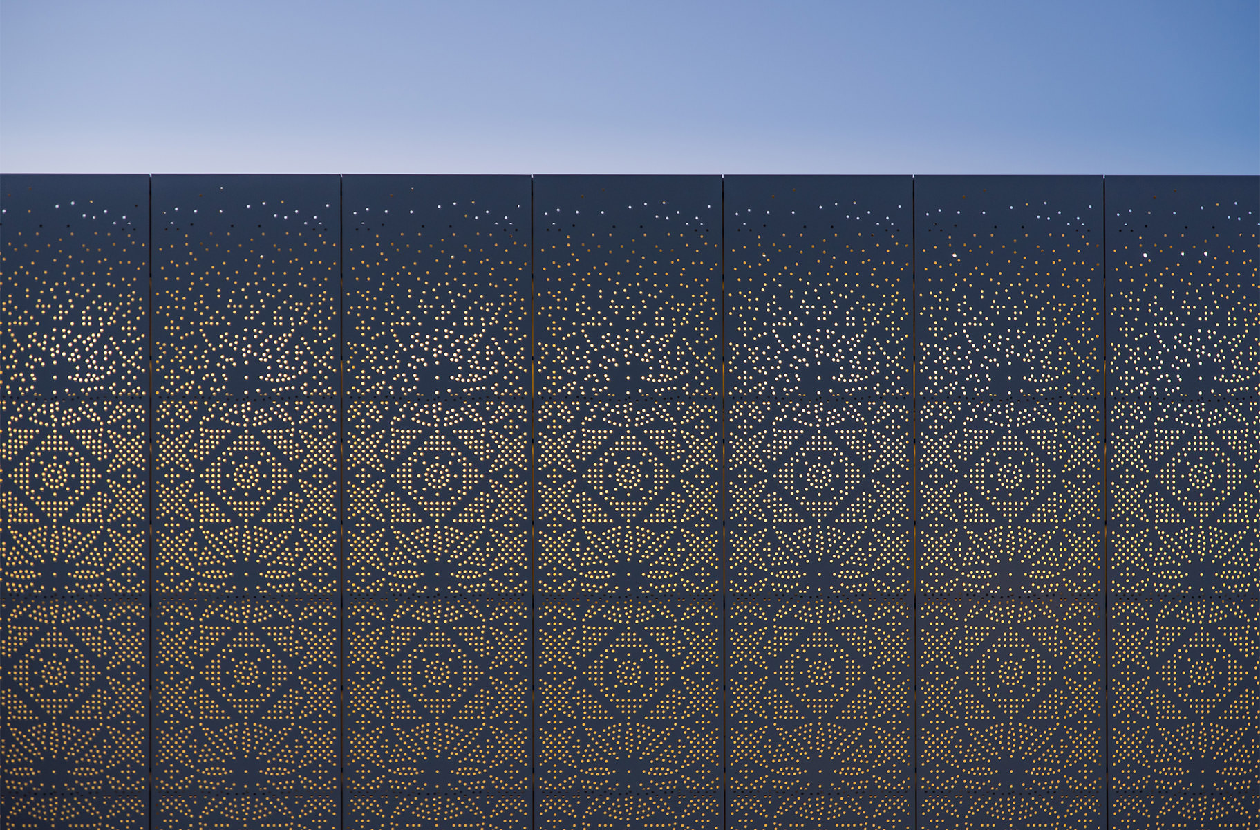 Photographie au crépuscule d'un détail de la façade perforée qui laisse apparaître des motifs en arabesques