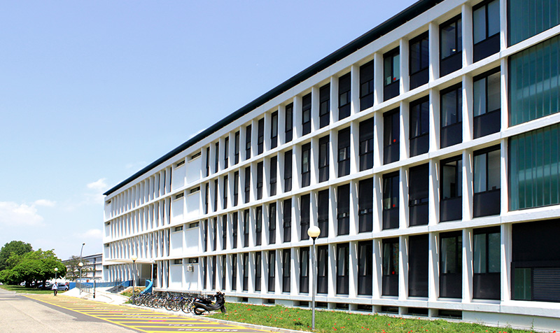 Photographie trois quart du bâtiment tout en longueur, mur blanc et ouvertures vitrées en renfoncement, menuiseries bleu foncé