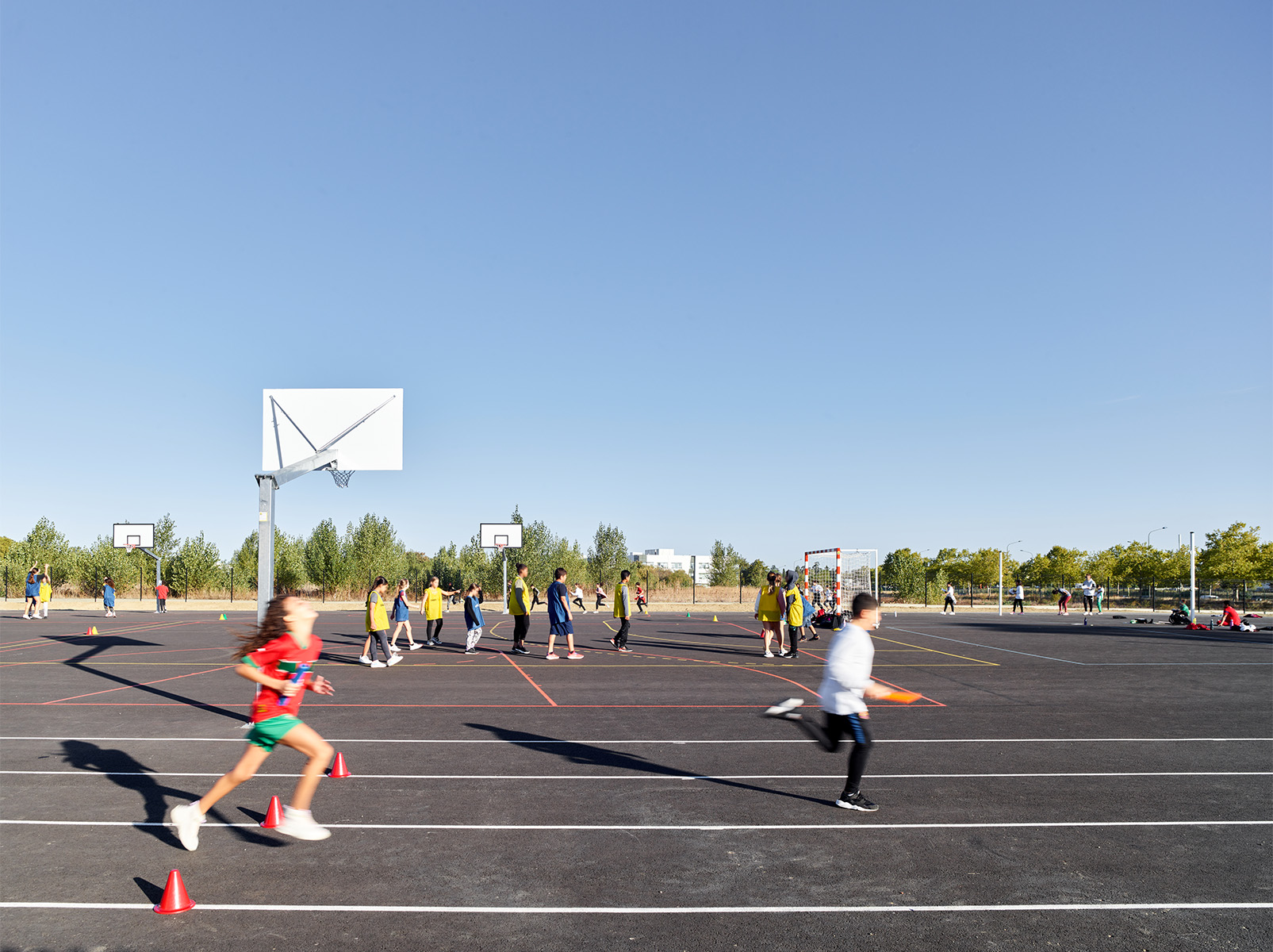 Photographie des terrains de sport, avec plusieurs classes en train de faire du sport, vue vers les espaces verts