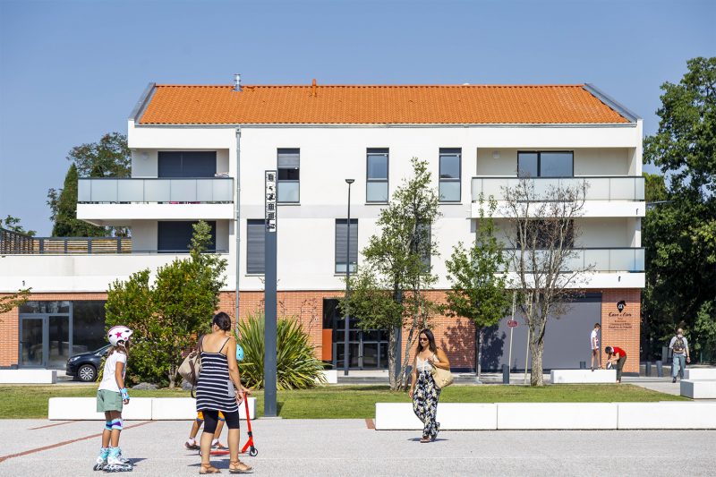 Photographie de la vie de quartier devant les logements, place de la mairie en premier plan