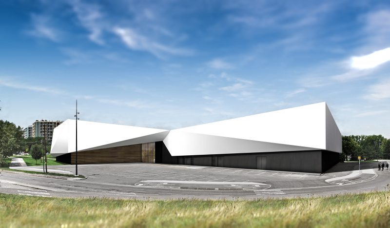 Perpective de l'ensemble du bâtiment depuis l'espace végétalisé de l'autre côté de la route, façades blanches en origami et soubassement en lames de bois