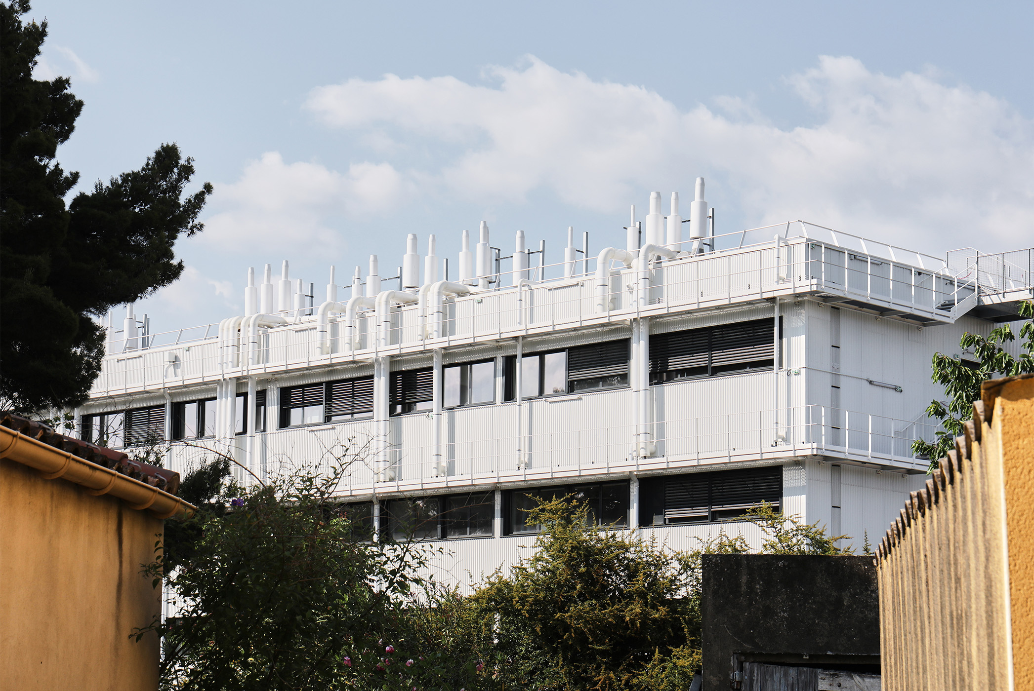 Photographie de loin de l'arrière du bâtiment, des équipements techniques en toiture relient les étages