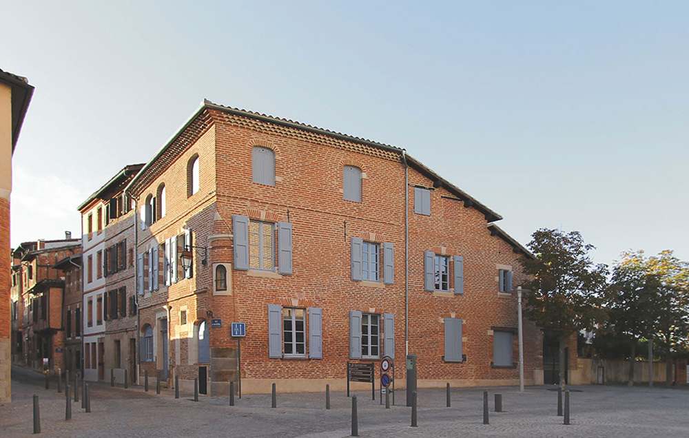 Photographie du bâtiment en R+2 rénové tout en brique et volets bleu lavande