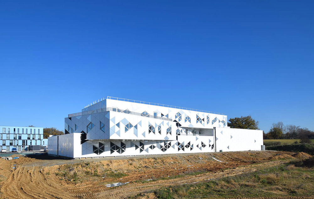 Photographie depuis l'espace vert en chantier dans le bâtiment, façades avec motifs et fenêtres triangulaire bien avancé