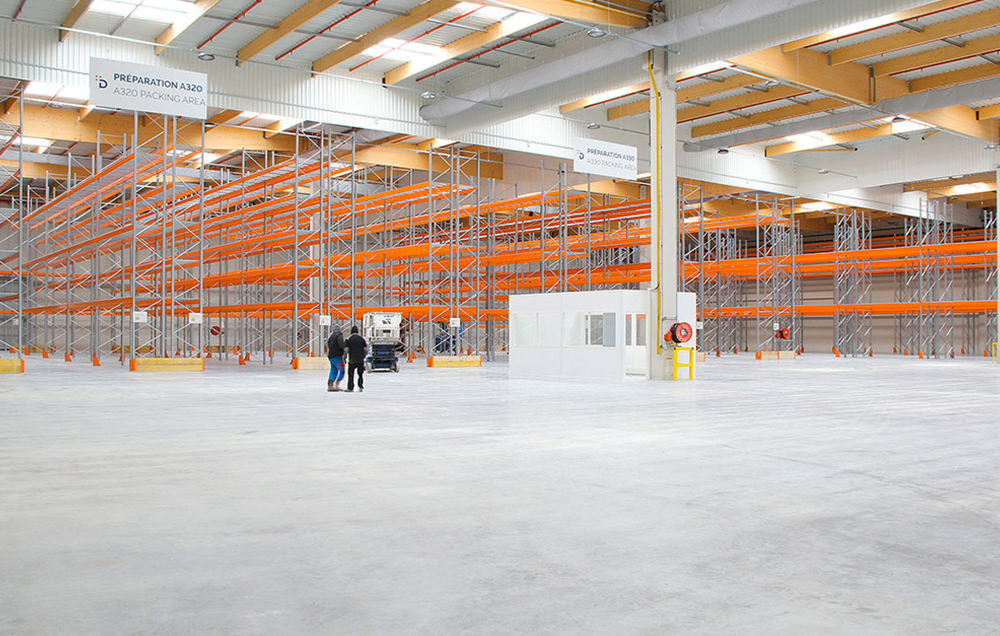 Photographie de l'intérieur du bâtiment, avec en fond tous les racks de stockage orange
