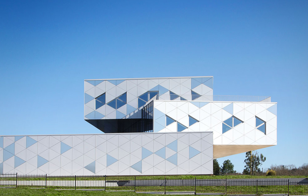 Photographie des trois faces du bâtiment orienté différement, fenêtres et motifs triangulaires qui reflétent le ciel bleu