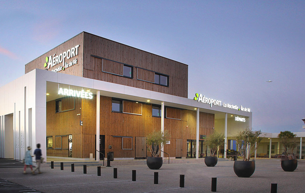 Photographie du parvis de l'aéroport, bâtiment en lames de bois et auvent blanc