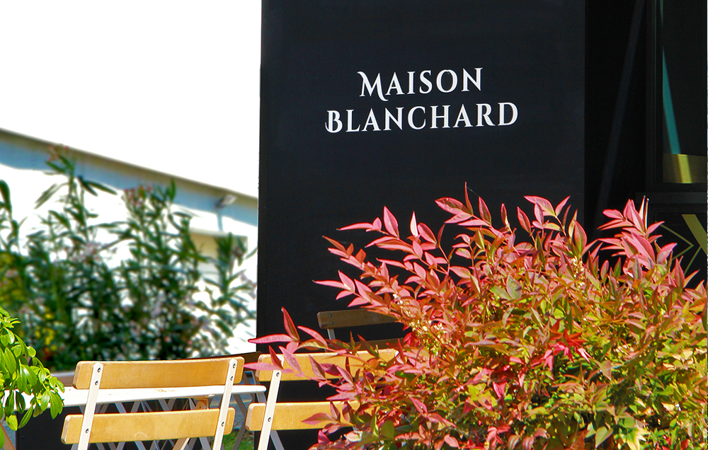 Photographie d'un détail de la boutique, vue sur la terrasse, le logo Maison Blanchard en blanc sur la boulangerie noire