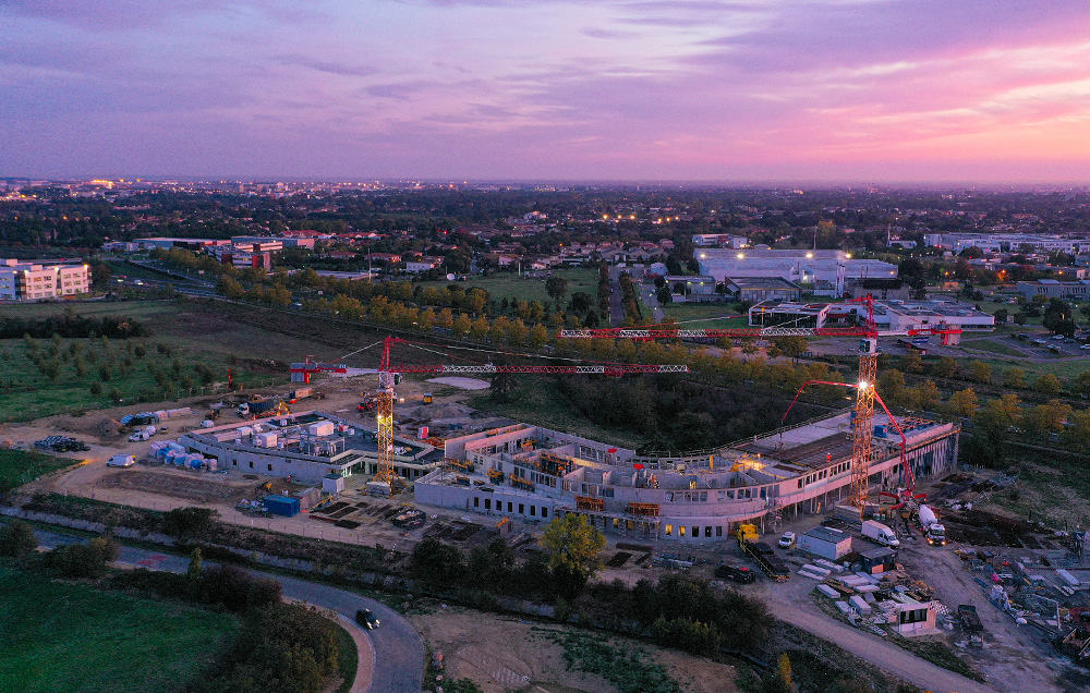 Photographie de drone du chantier de Guilhermy, on voit la structure en béton et les deux grues sur fond de couché de soleil