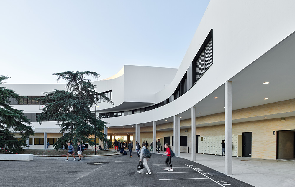 Photographie de la cour du collège avec les éléves qui arrivent, batiment qui englobent, en courbe sur deux niveaux différents, les 2 cèdres