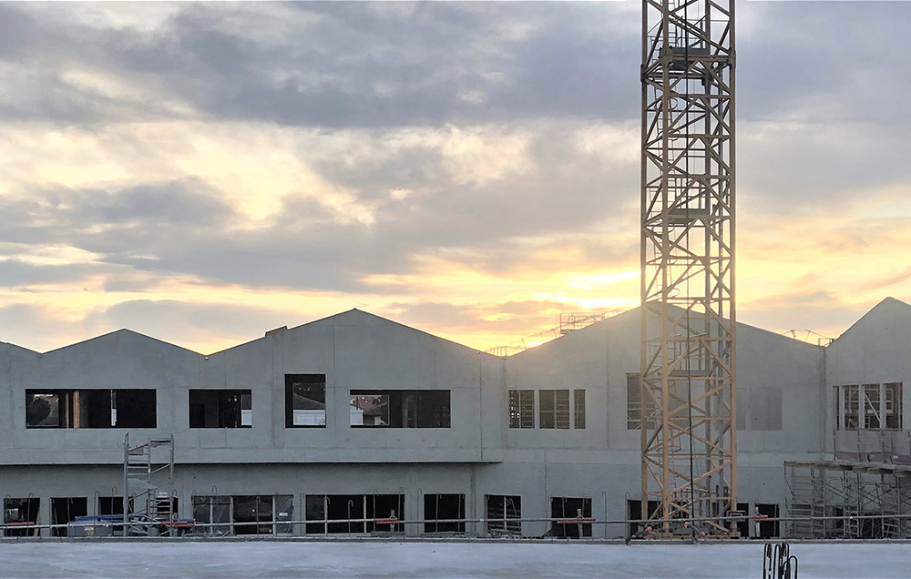 Photographie de chantier de l'école Josephine baker, une grue au 1er plan et on peut deja lire la structure béton du batiment et ses toitures en pente douce