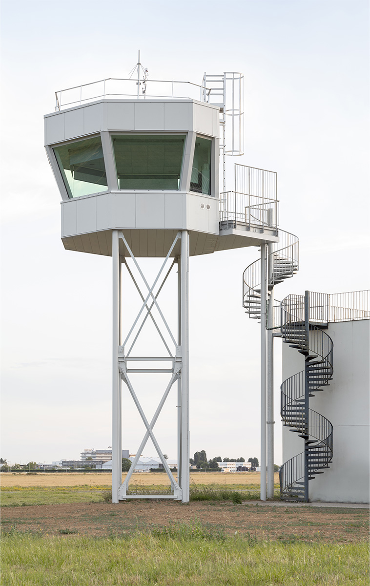 Photographie verticale de la vigie de Melun-Villaroche et ses deux escaliers en colimaçon pour y accèder, le 1er mène à la toiture du bâtiment adjacent pour ensuite prendre le 2eme qui monte à la vigie