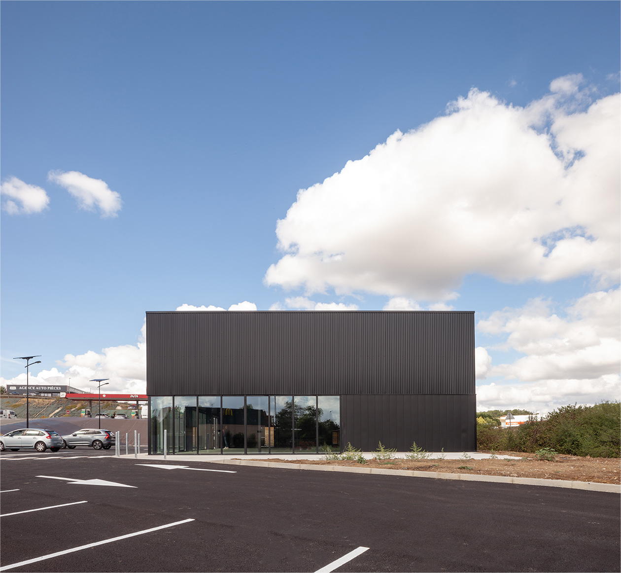 Photographie face à la largeur de la coque commerciale à Foulayronnes, vue depuis le parking, bâtiment tout gris anthracite, bardage serré en haut et espacé en bas, en partie basse 60% vitré