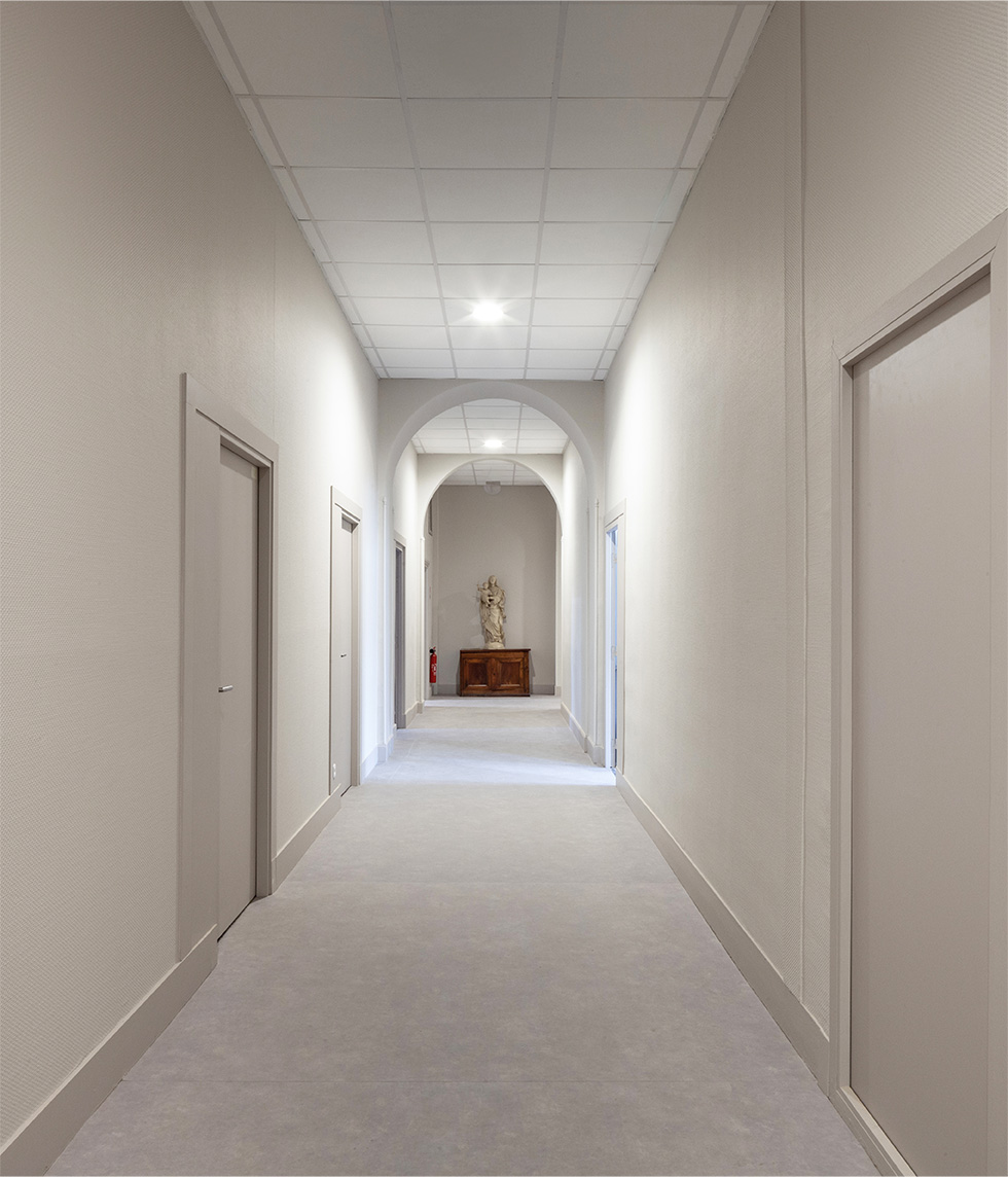 Photographie d'un couloir blanc avec le rappel des courbes du cloitres au niveau du faux plafond blanc avec deux voutes blanches