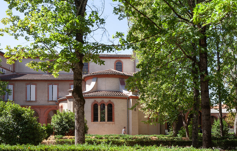 Photographie depuis le jardin vue sur le diocèse d'Albi en arrière plan entre les grands arbres et plusieurs rangé de haies et d'arbustes sur le côté